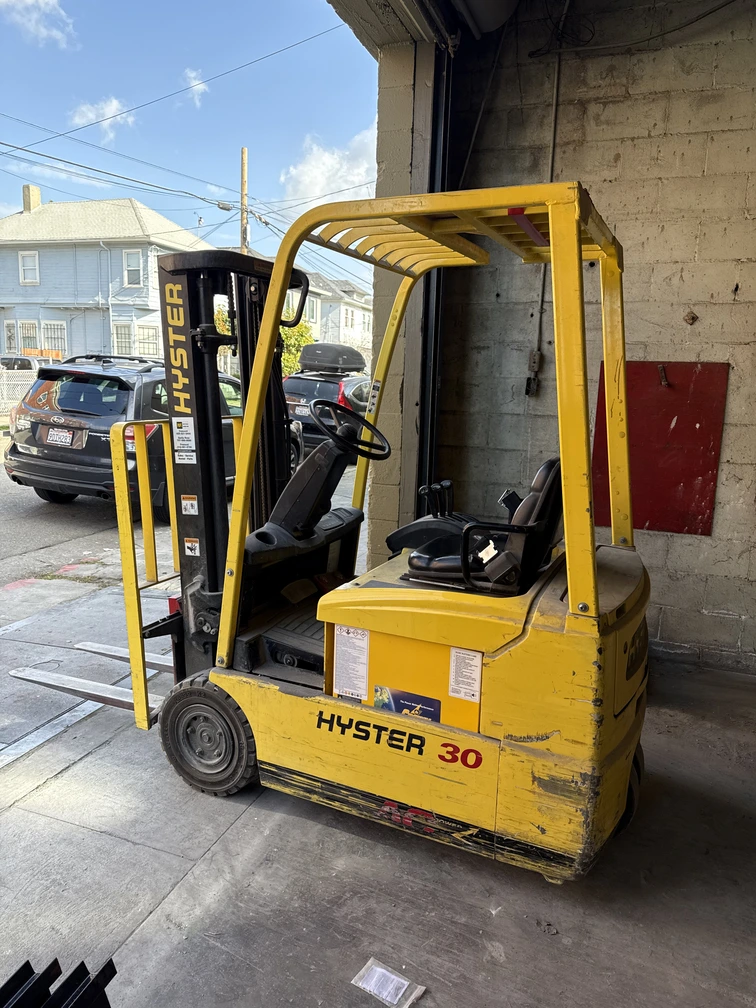 Yellow Hyster 30 electric forklift parked in a warehouse loading bay with visible forks and operator seat.